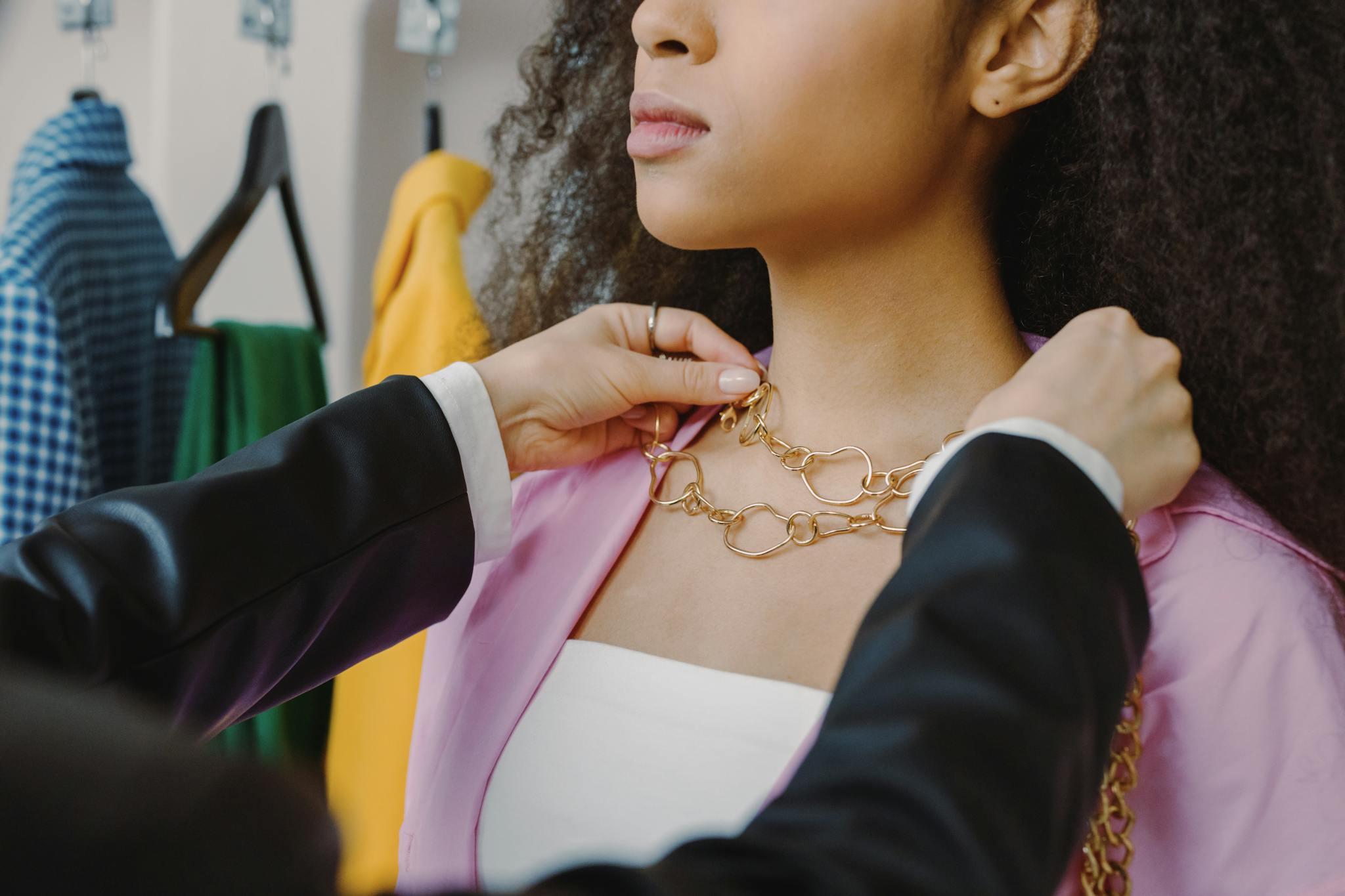 Close-up of a woman trying on a gold necklace in a trendy fashion store setting.