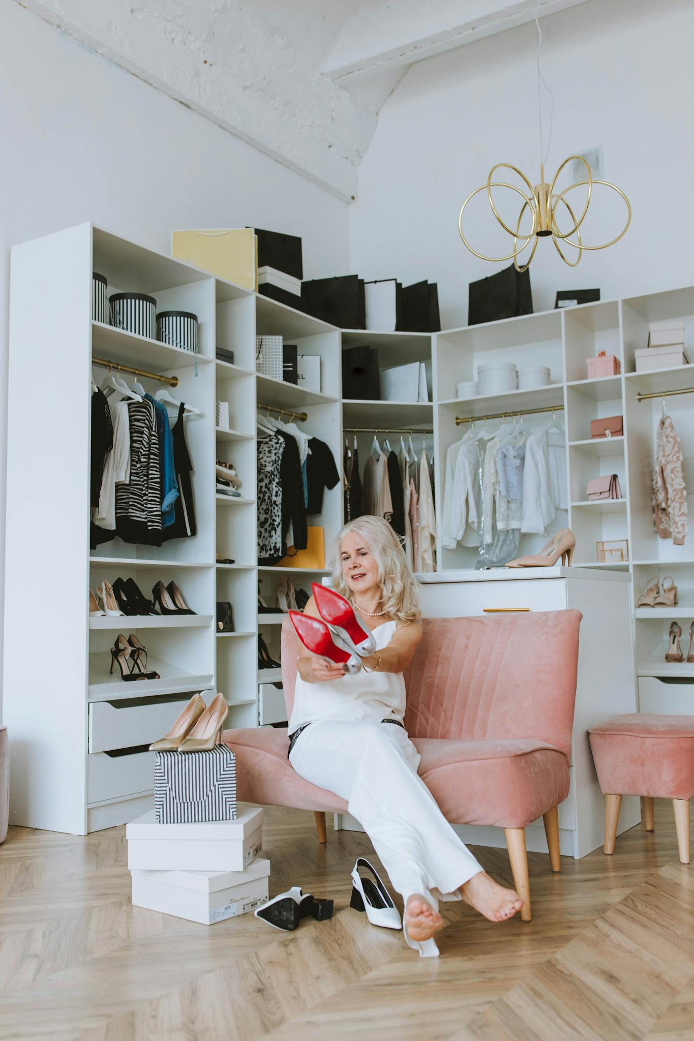 Senior woman enjoying her stylish wardrobe, surrounded by clothes and shoes at home.